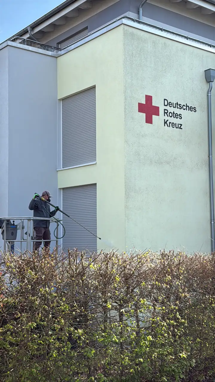 Fassade eines Seniorenheims mit Algenbelag während der Niederdruckreinigung von der Arbeitsbühne