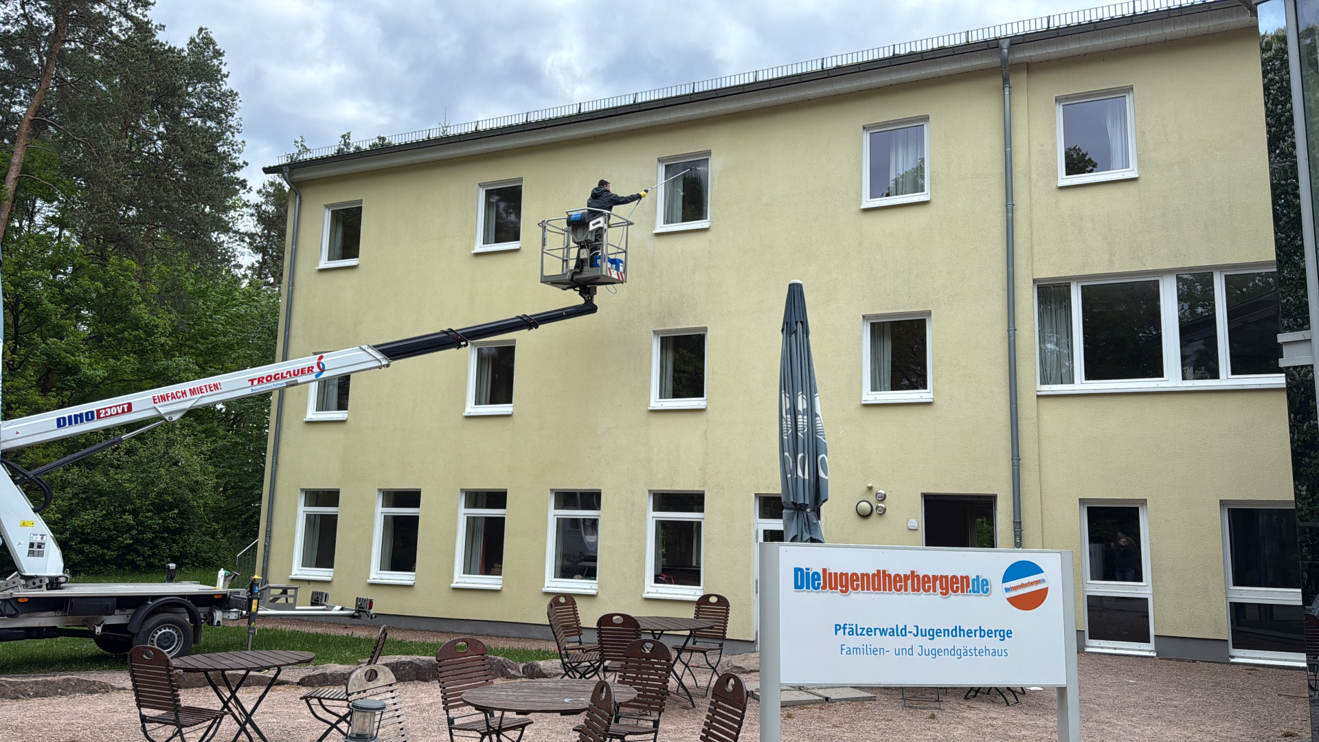 Mitarbeiter reinigt die Putzfassade der Pfälzerwald-Jugendherberge Hochspeyer von einer Hebebühne aus