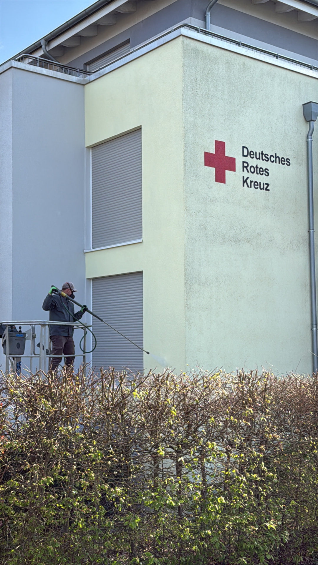 Fassade eines Seniorenheims mit Algenbelag während der Niederdruckreinigung von der Arbeitsbühne