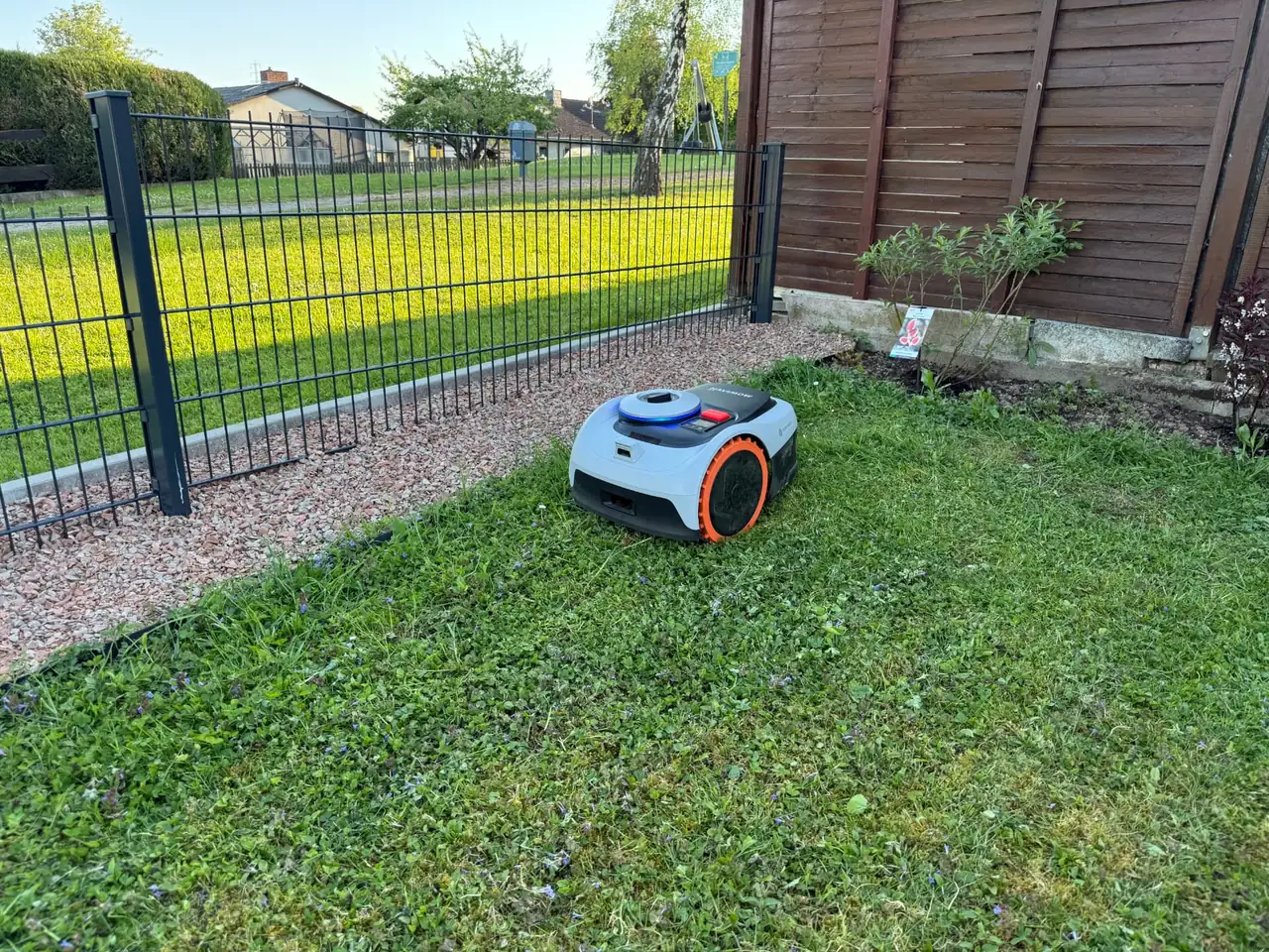 Navimow Mähroboter auf der Rasenfläche neben neuer Zaunanlage mit Kiesstreifen