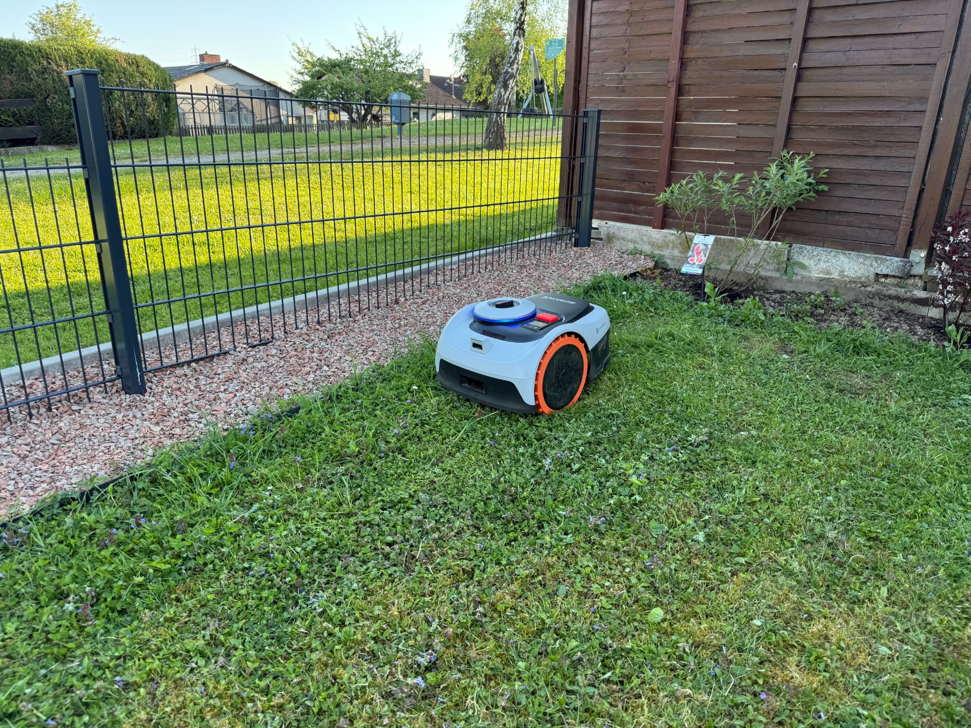 Navimow Mähroboter auf der Rasenfläche neben neuer Zaunanlage mit Kiesstreifen