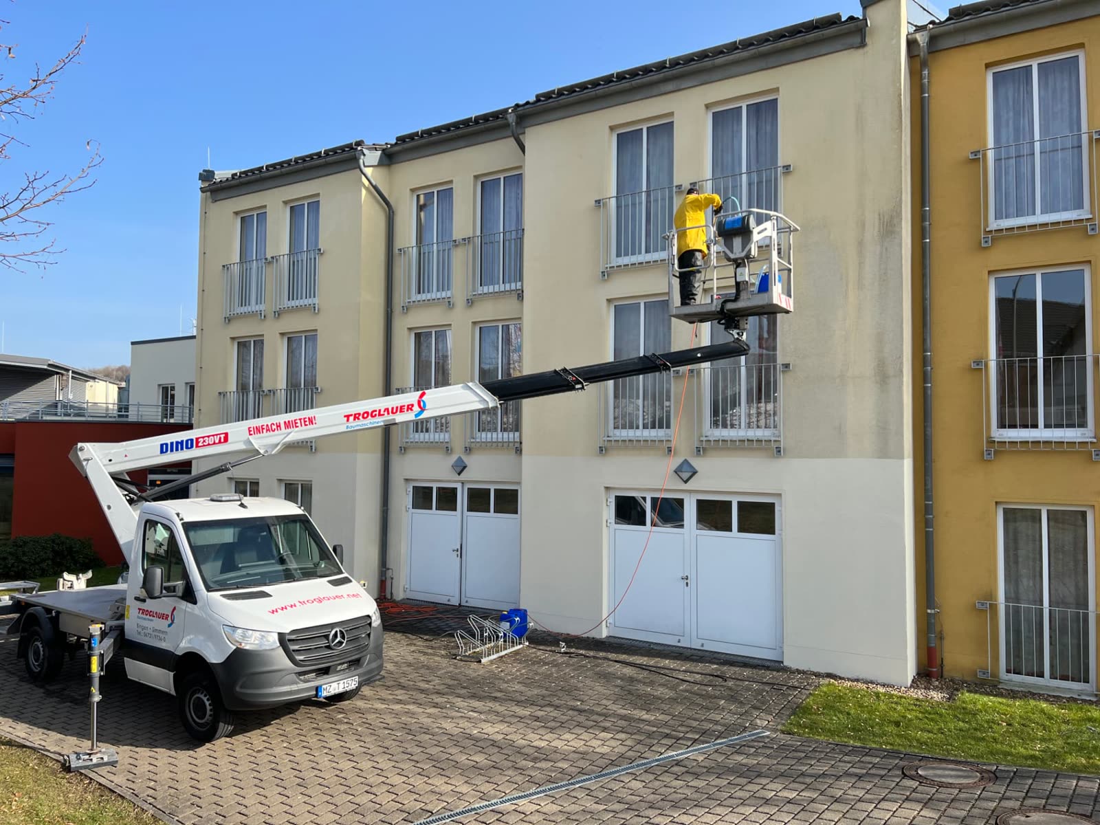 Mitarbeiter reinigt die Fassade der Jugendherberge Prüm von einer Anhänger-Hebebühne aus